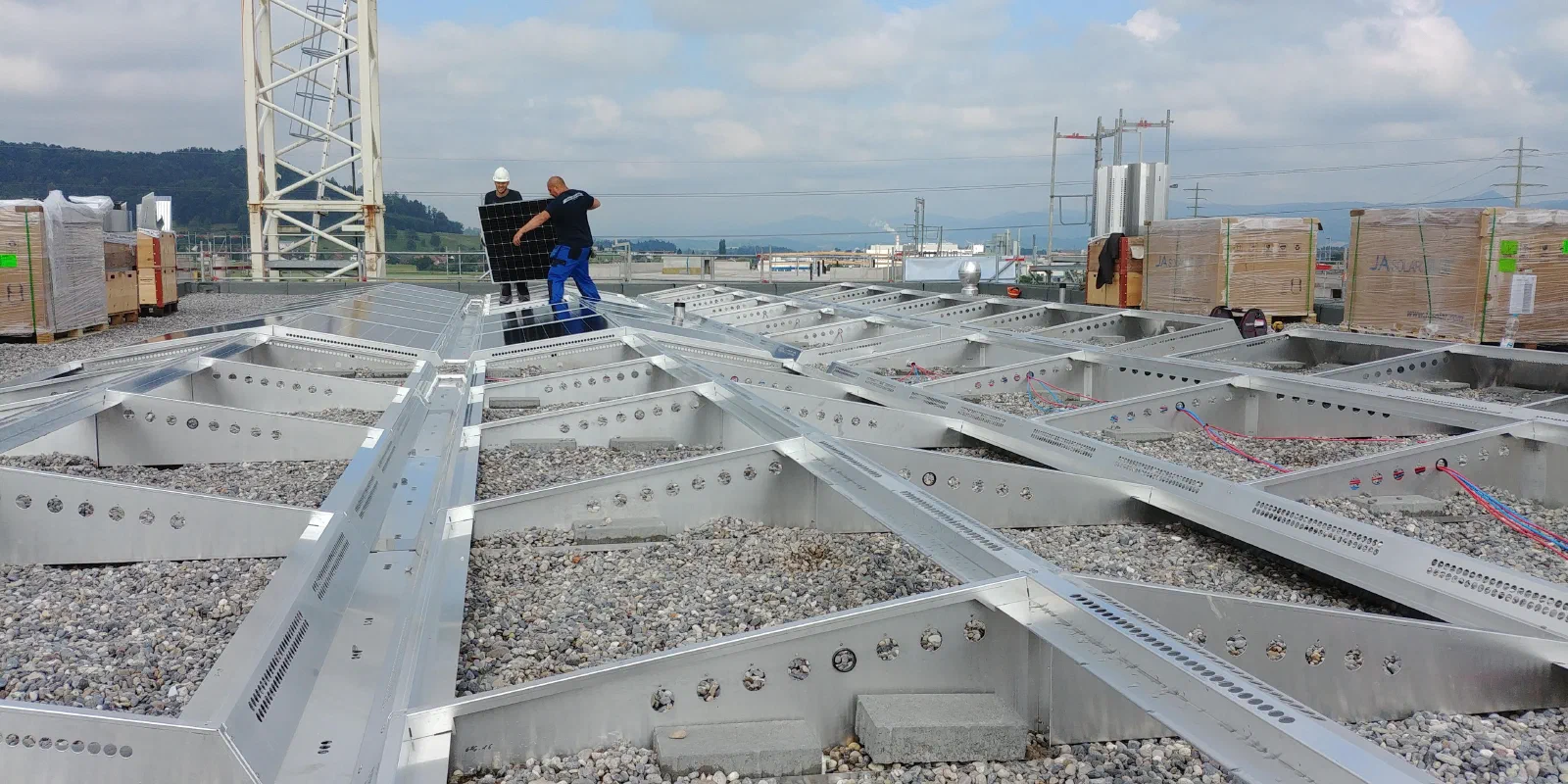 Aluminium-Unterkonstruktion auf dem Kiesdach von Haus B2, im Hintergrund zwei Monteure mit einem Modul