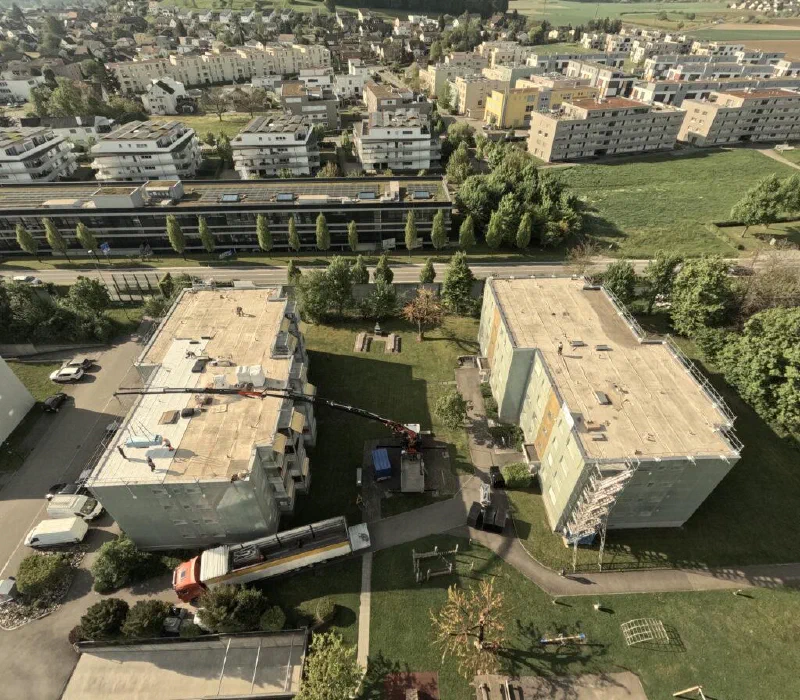 Luftaufnahme: Ein Kran hebt Material auf das Dach des linken Gebäudes