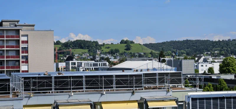 Blick über das Dach mit den vertikalen Solarmodulen, im Hintergrund grüne Hügel
