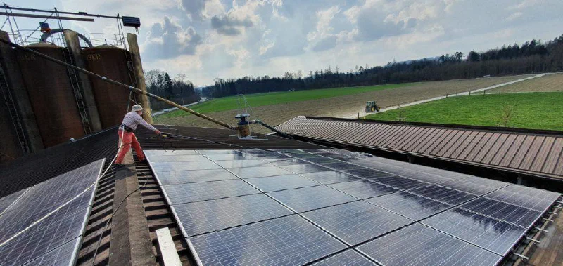 Ein Helfer reinigt die Module auf dem Scheunendach mit einer langen Bürste